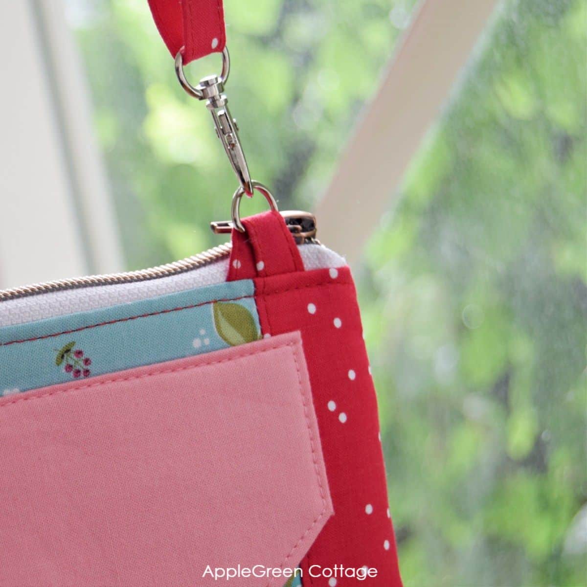 A beautiful red, light blue and floral printed quilting cotton zipper bag wallet hanging on a strap anchor modified to reduce bulk in sewing bag layers.