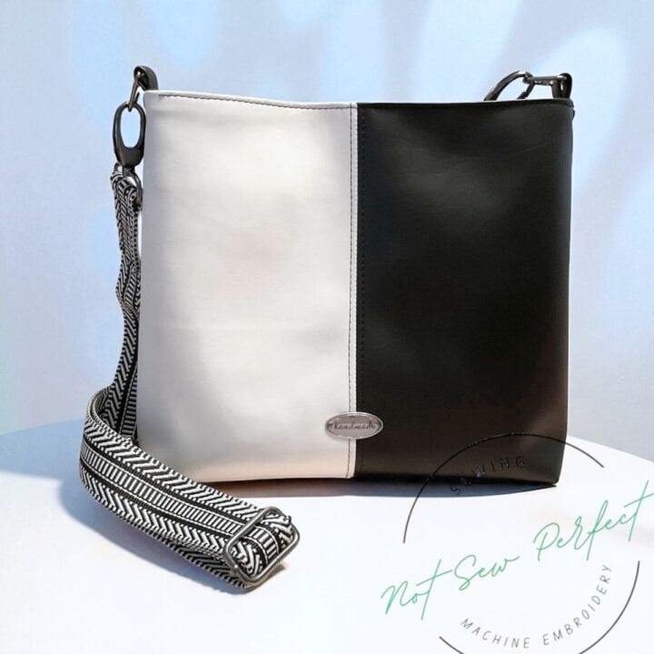 a finished color-blocked shoulder bag in white and black faux leather with a webbing strap.