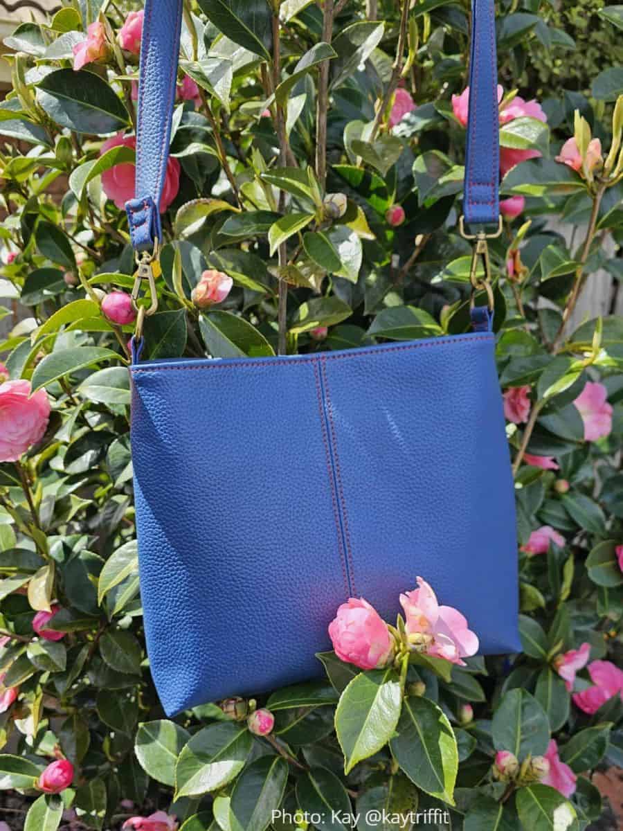 Blue faux leather Lumera bag with red contrast stitching and brass hardware.