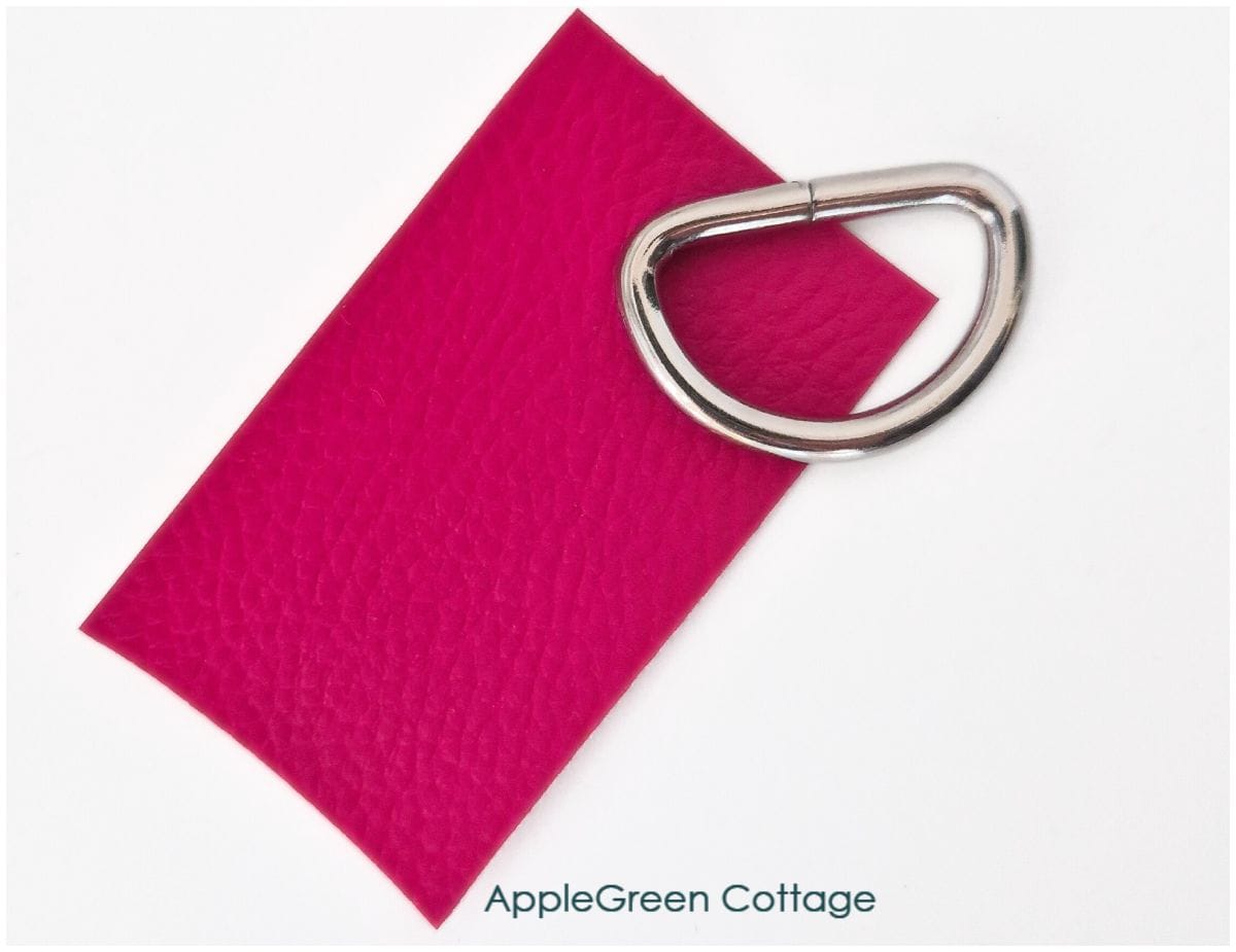 Faux leather rectangle and metal D-ring ready for a strap connector sewing step.
