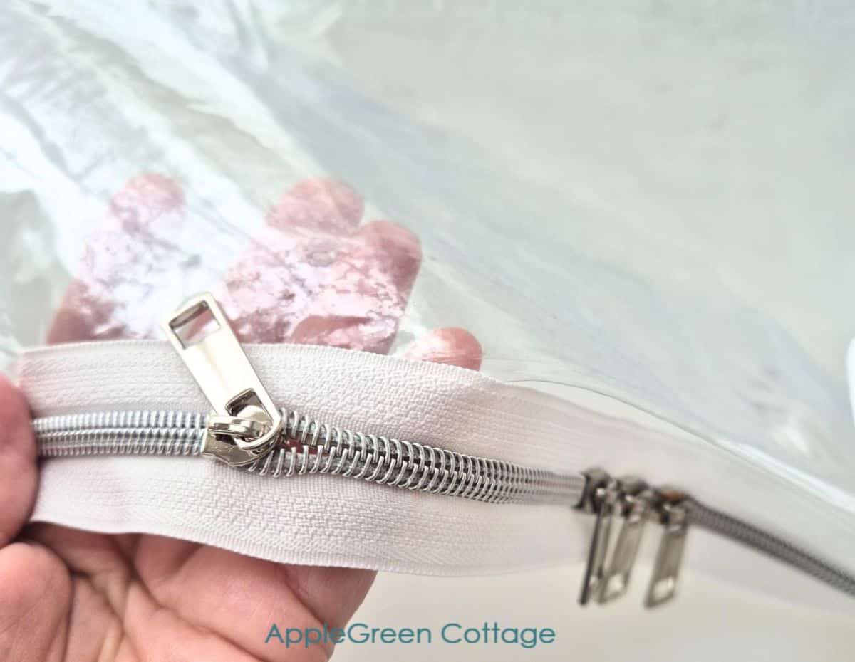 Clear vinyl zippered pouch sewing step showing zipper tape and metal slider.