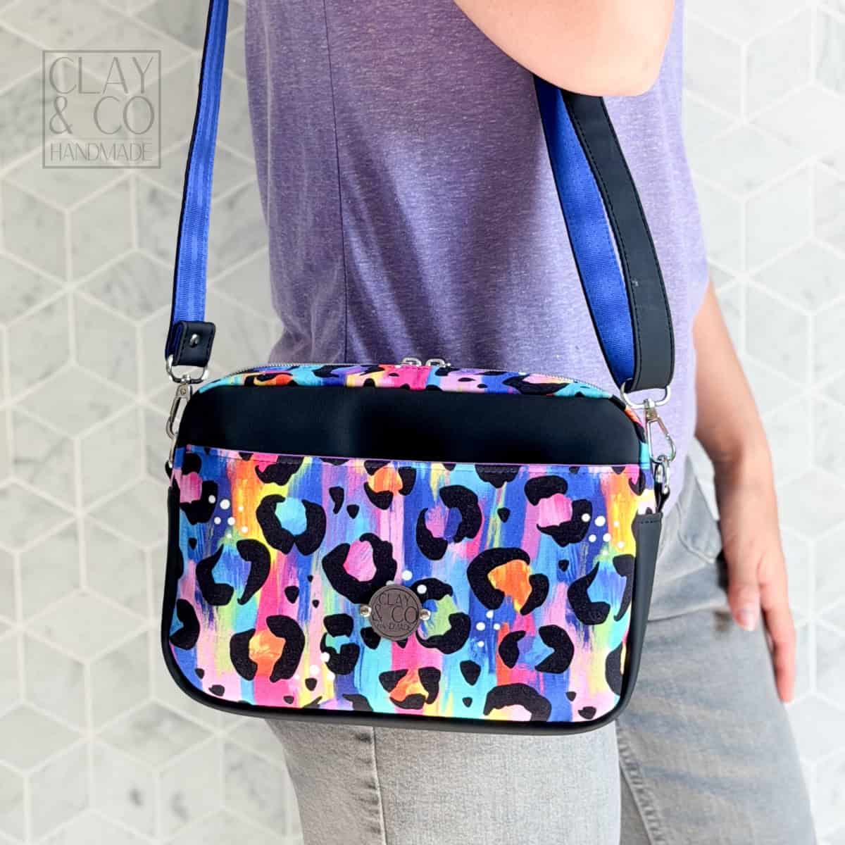 Crossbody bag made with vinyl exterior and zipper top, shown from side with boxed corners.