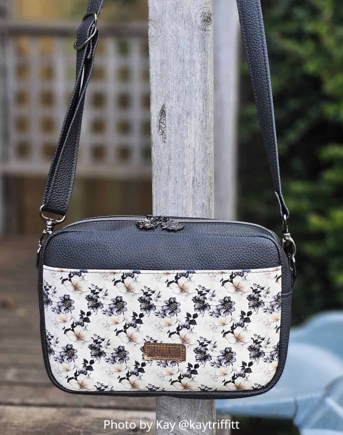 Close-up of faux leather, boxed-shape crossbody bag with a gusset, showing zipper installation, D-ring, swivel hook, and strap connector.