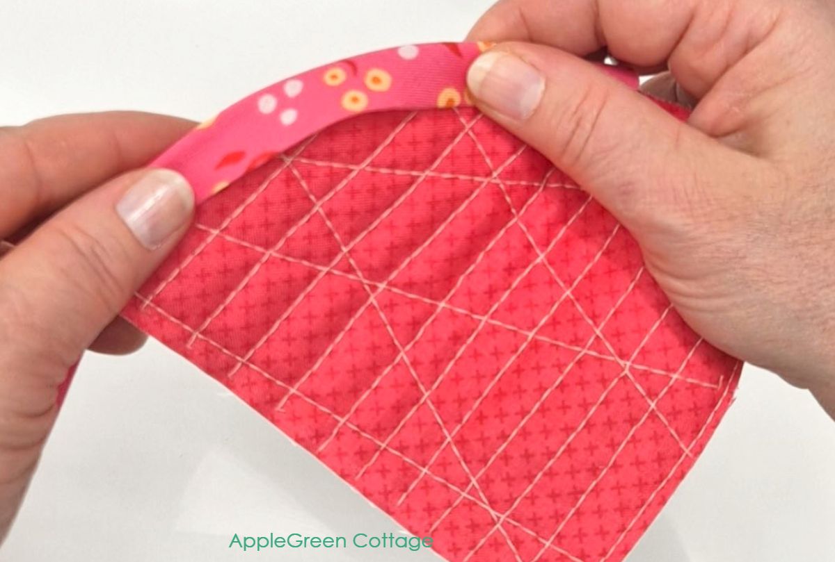 Folding bias tape over curved quilt edge by hand to check fit before topstitching.