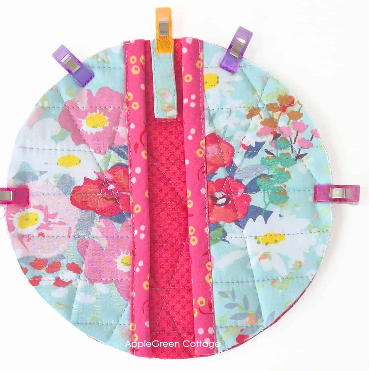 Round potholder back with hanging loop and pocket edges clipped before binding sewing step.