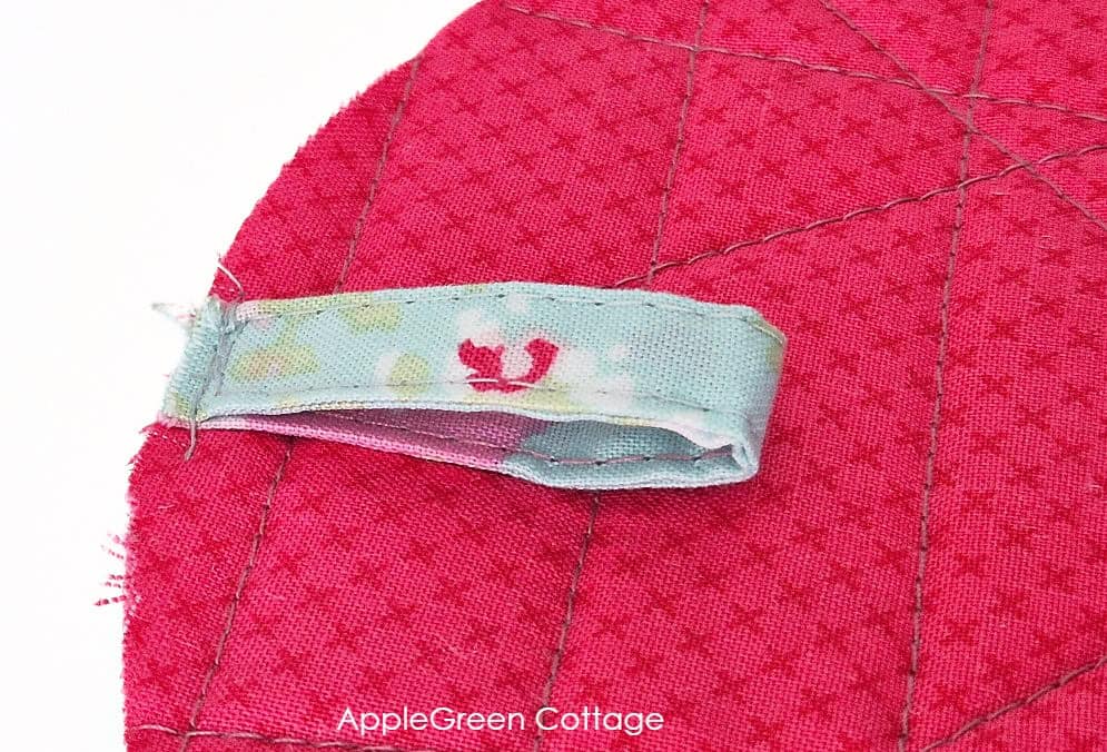Fabric hanging loop basted to quilted round potholder back before assembly.