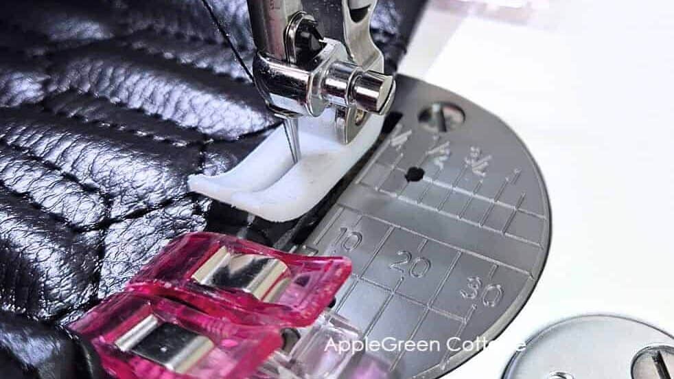 Janome Hd9 needleplate closeup showing Janome's ultra glide machine foot sewing over several layers of black vinyl, clipped together using wonder clips.